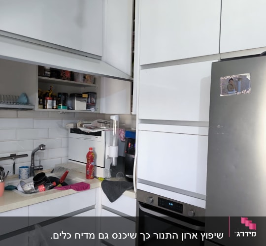 מטבח עם ארונות לבנים, כיור ותנור אפייה.